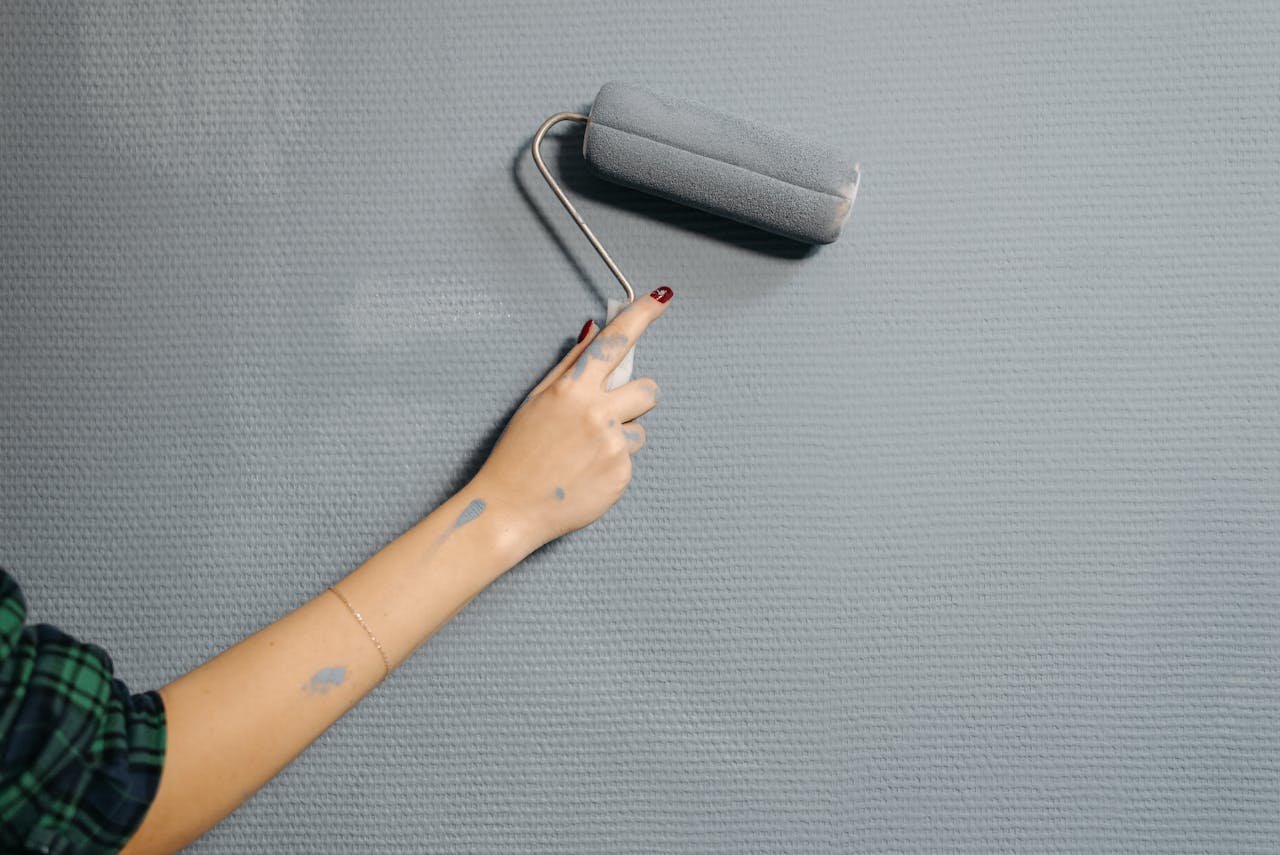 why-choose-us-img A close-up of a persons hand using a paint roller on a blue wall for home renovation.
